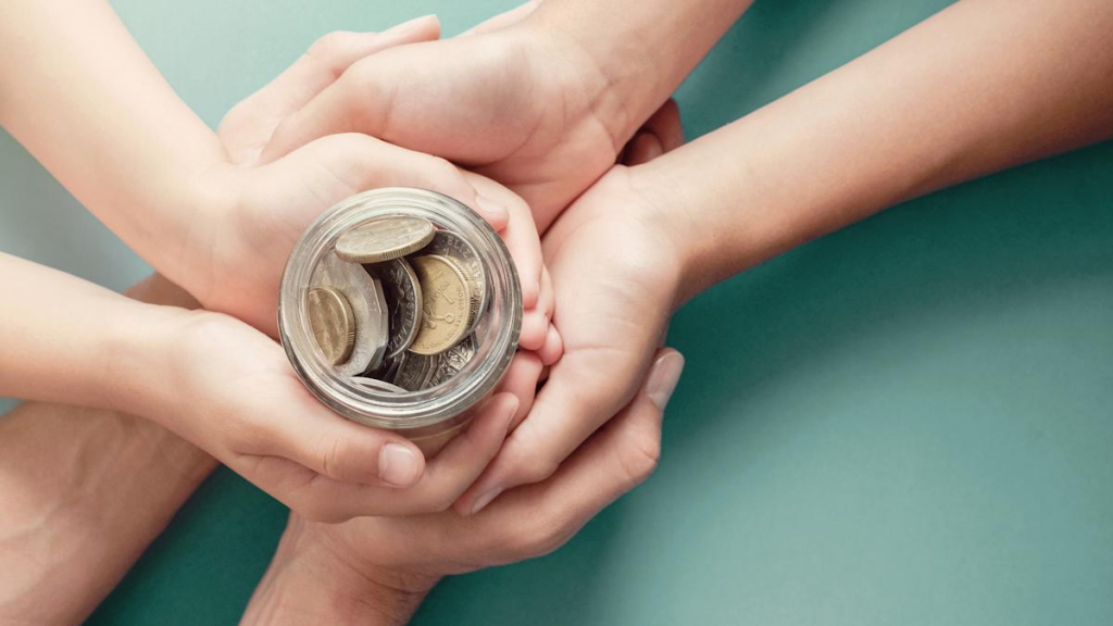 Three pairs of hands cradle a glass jar full of coins.
